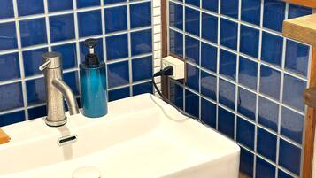 A white sink with a silver faucet, a blue soap dispenser, and a power outlet on a wooden countertop.