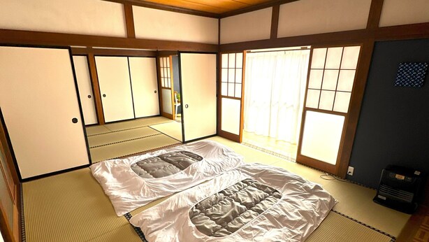 Una habitación con tatamis, una cama grande, puertas correderas y una lámpara de techo de estilo japonés tradicional.