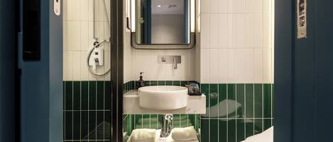 A bathroom with a white sink, green-tiled walls, a mirror, and a shower.