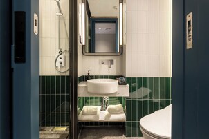 A bathroom with a white sink, green-tiled walls, a mirror, and a shower.