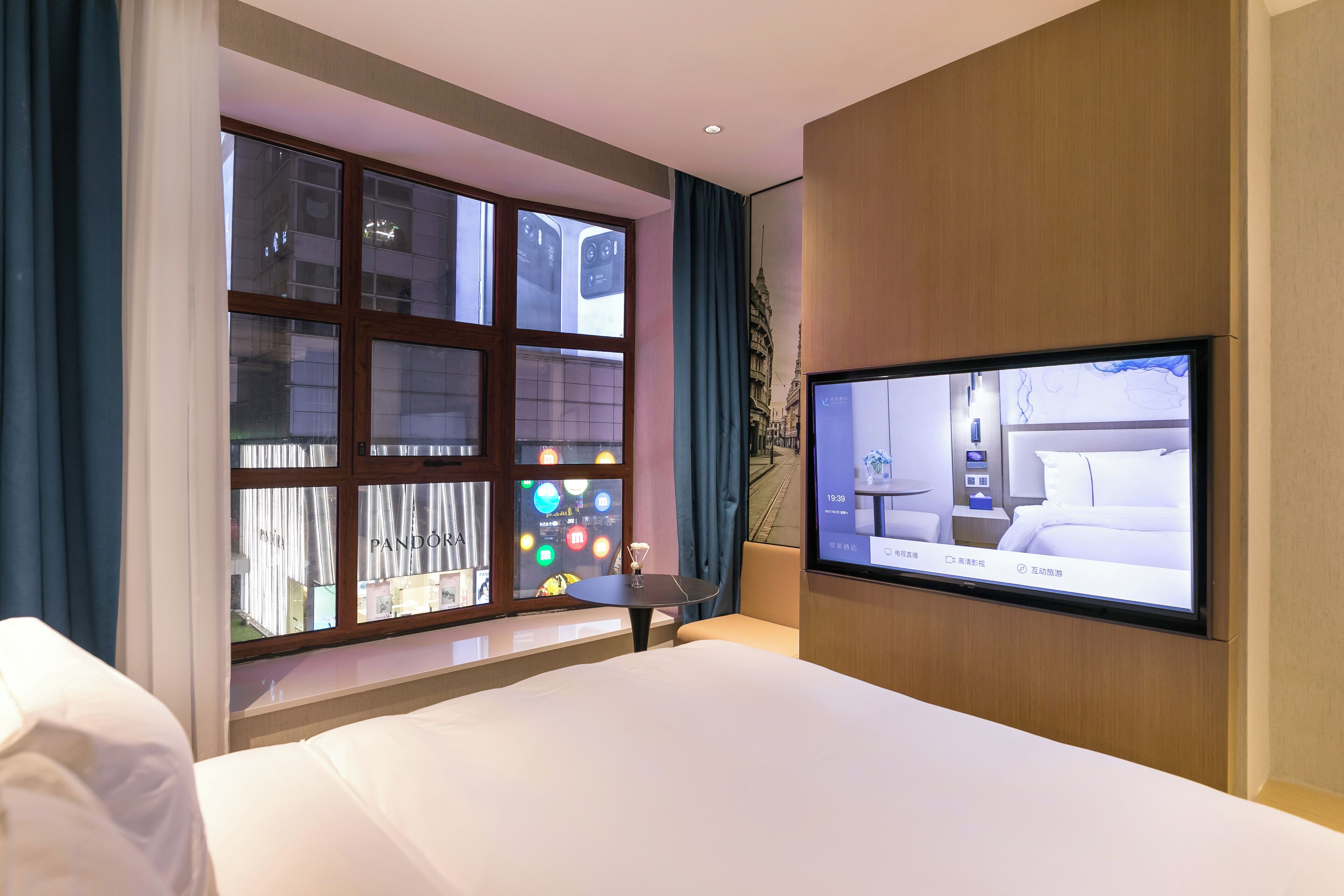 Habitación de hotel con un ventanal grande, un televisor de pantalla plana en la pared y una cama con ropa blanca.