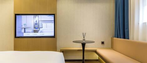 Habitación de hotel con cama, sofá, una mesita con un florero y un televisor montado en la pared.