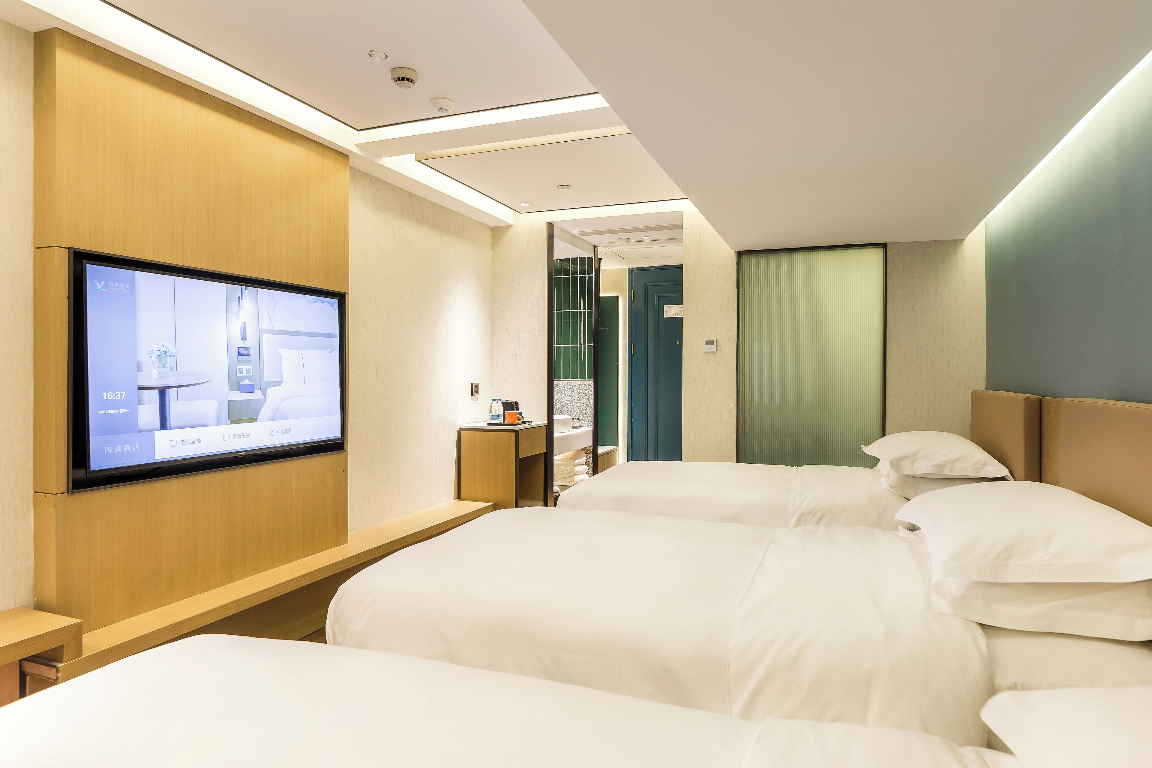 Hotelkamer met een grote flatscreen televisie aan de muur, een houten hoofdbord, twee bedden met witte beddengoed, een nachtkastje en een klein plankje met toiletartikelen.
