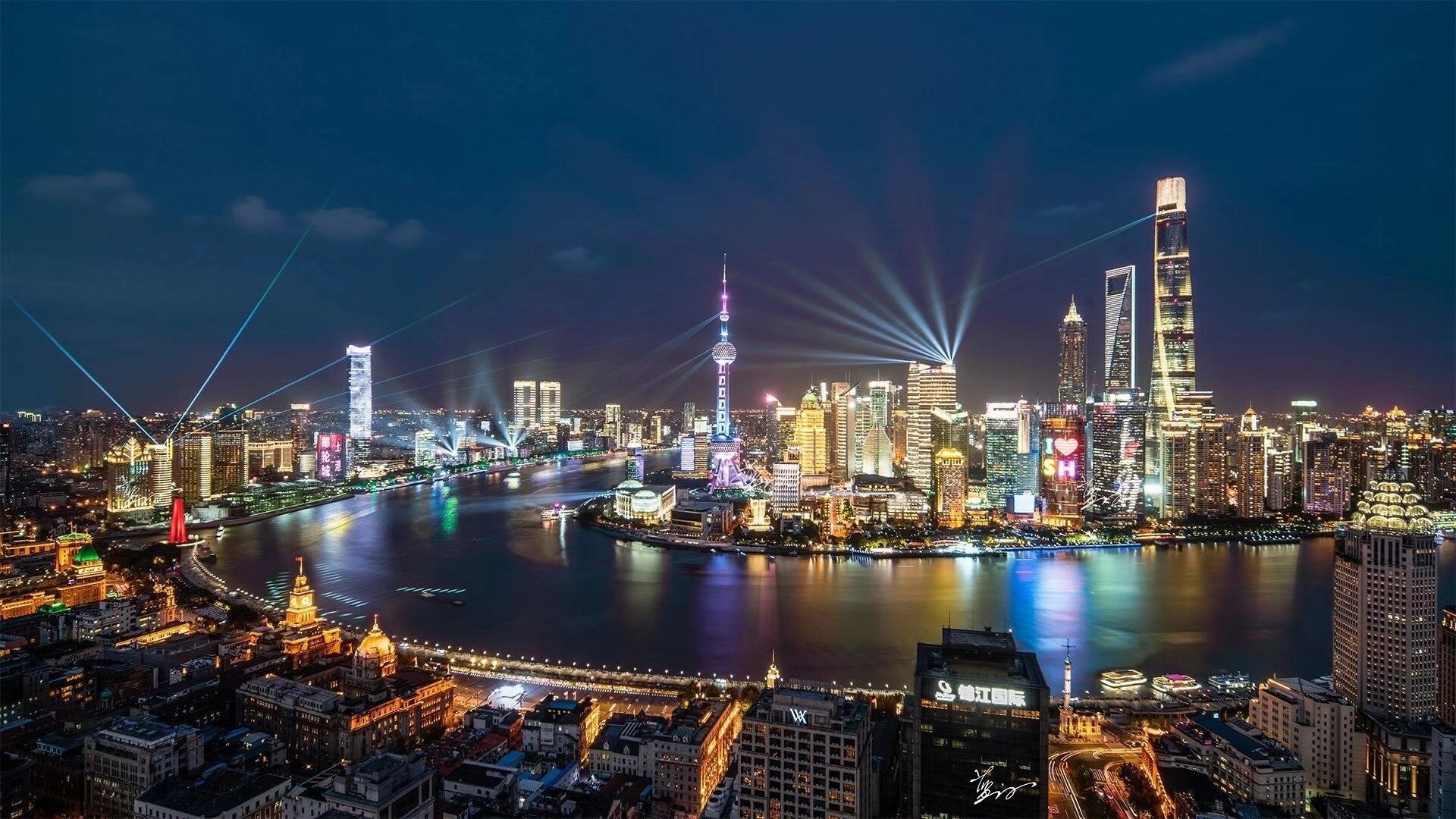 A nighttime cityscape with illuminated buildings and a river.