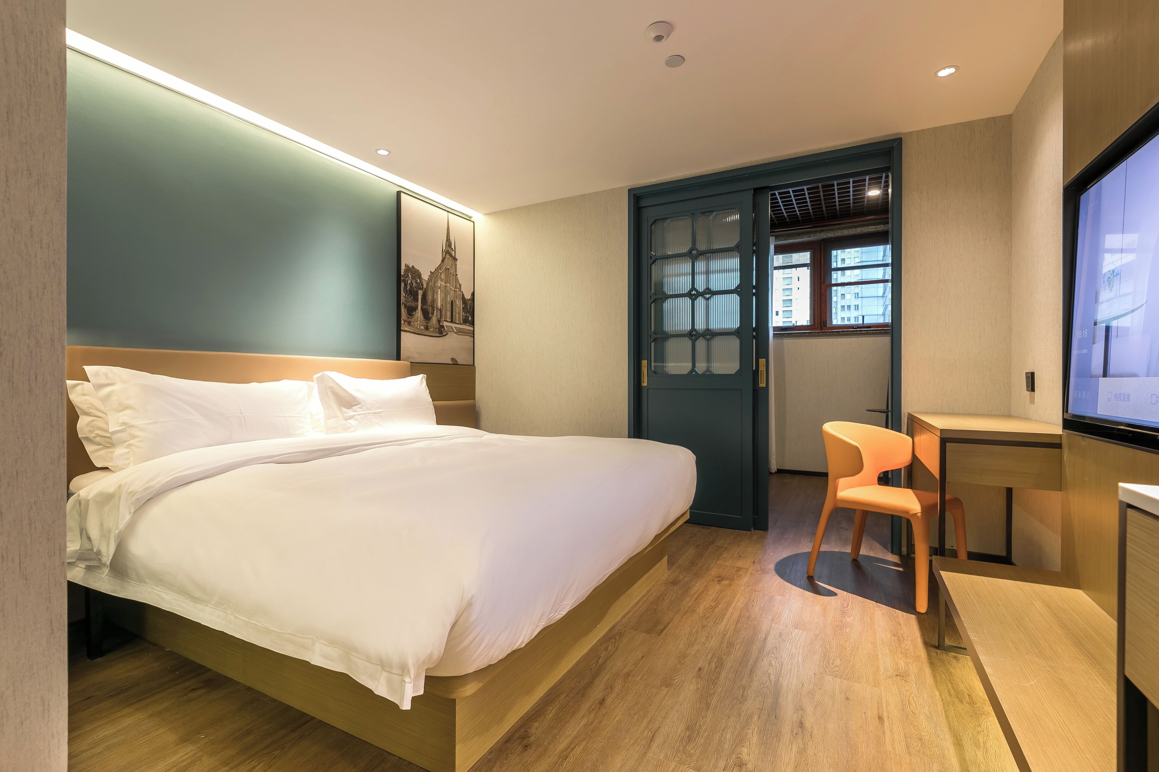 A modern hotel room with a large bed, a desk, a chair, and a television.