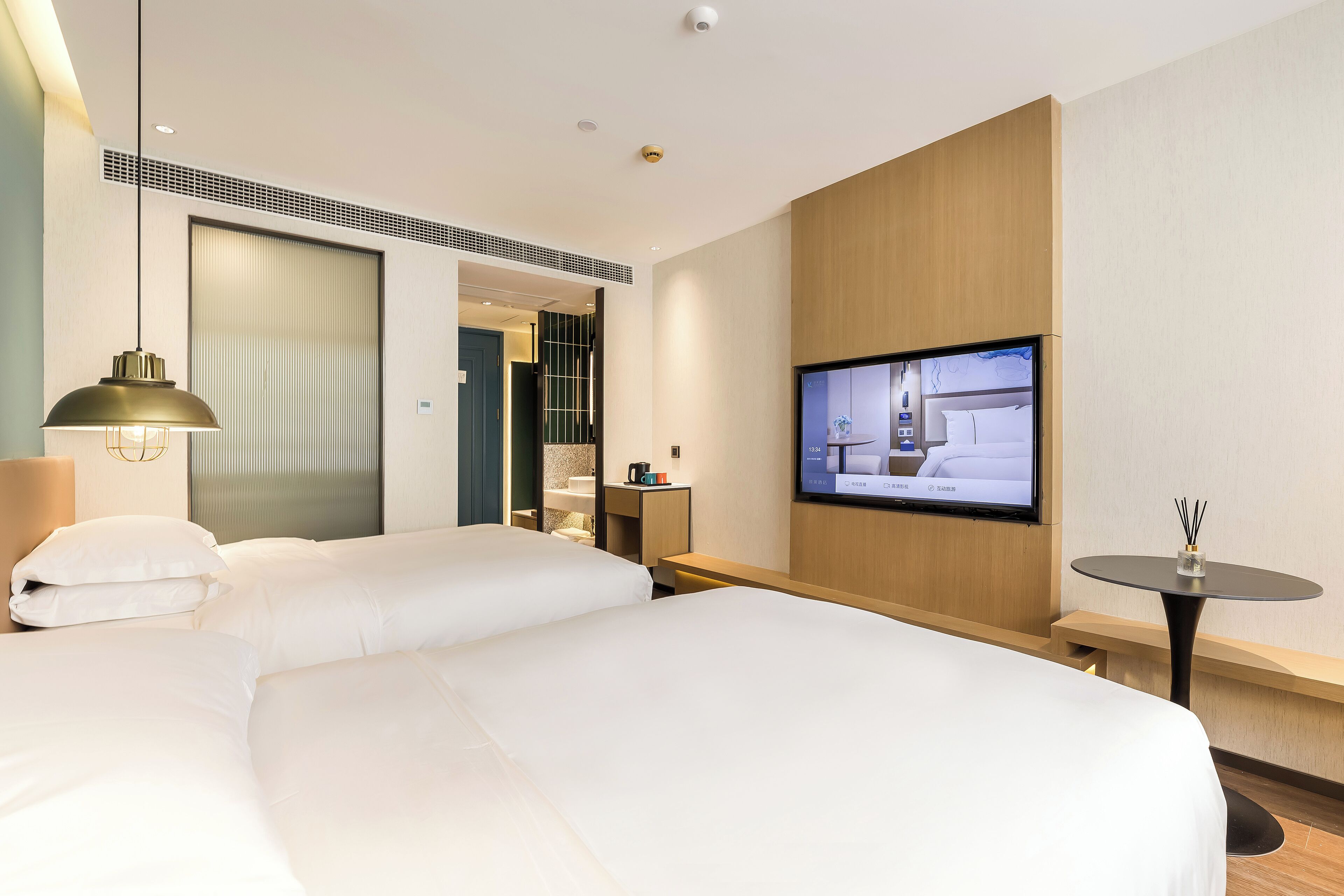 Una habitación de hotel con dos camas, televisión, una mesita y televisor montado en la pared.