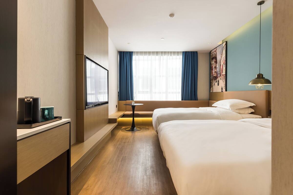 Une chambre d’hôtel avec deux lits, une petite table, un téléviseur et une fenêtre avec des rideaux.