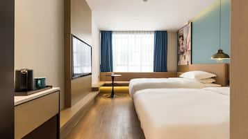 A hotel room with two beds, a small table, a TV, and a window with curtains.