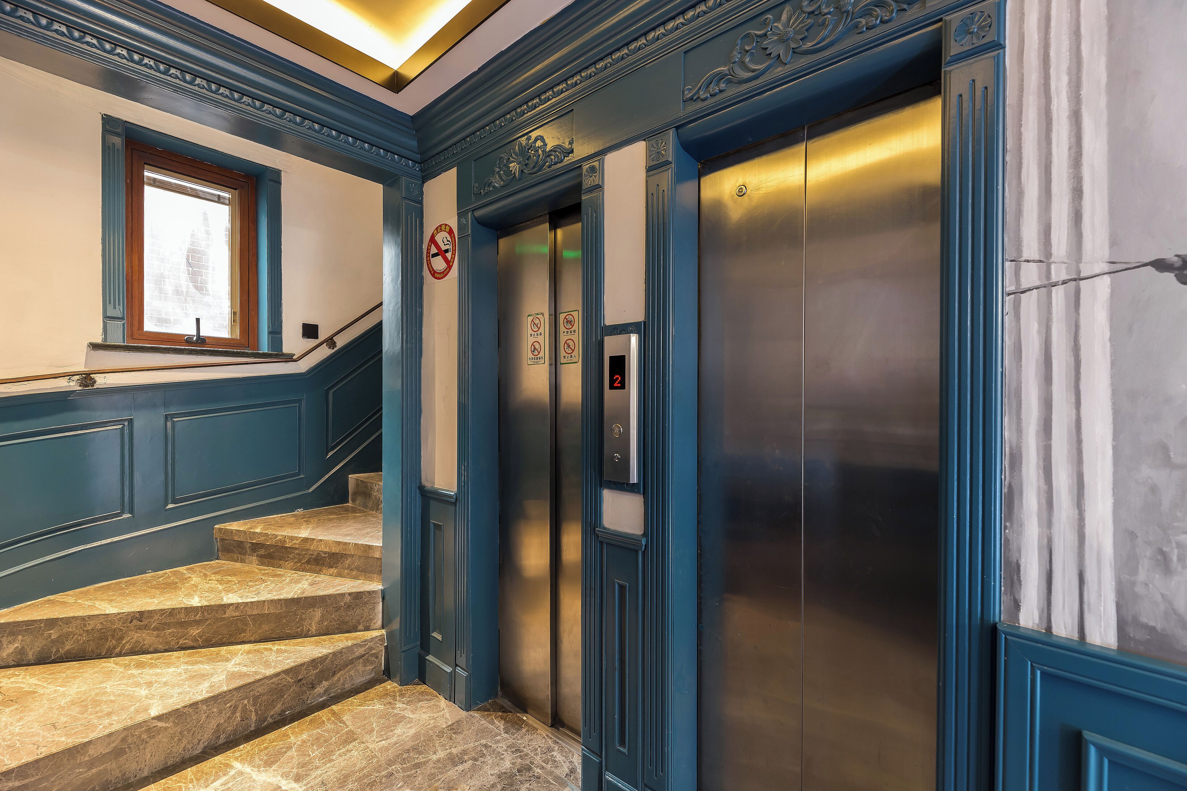 A staircase leading to an elevator with blue trim and a no-smoking sign.