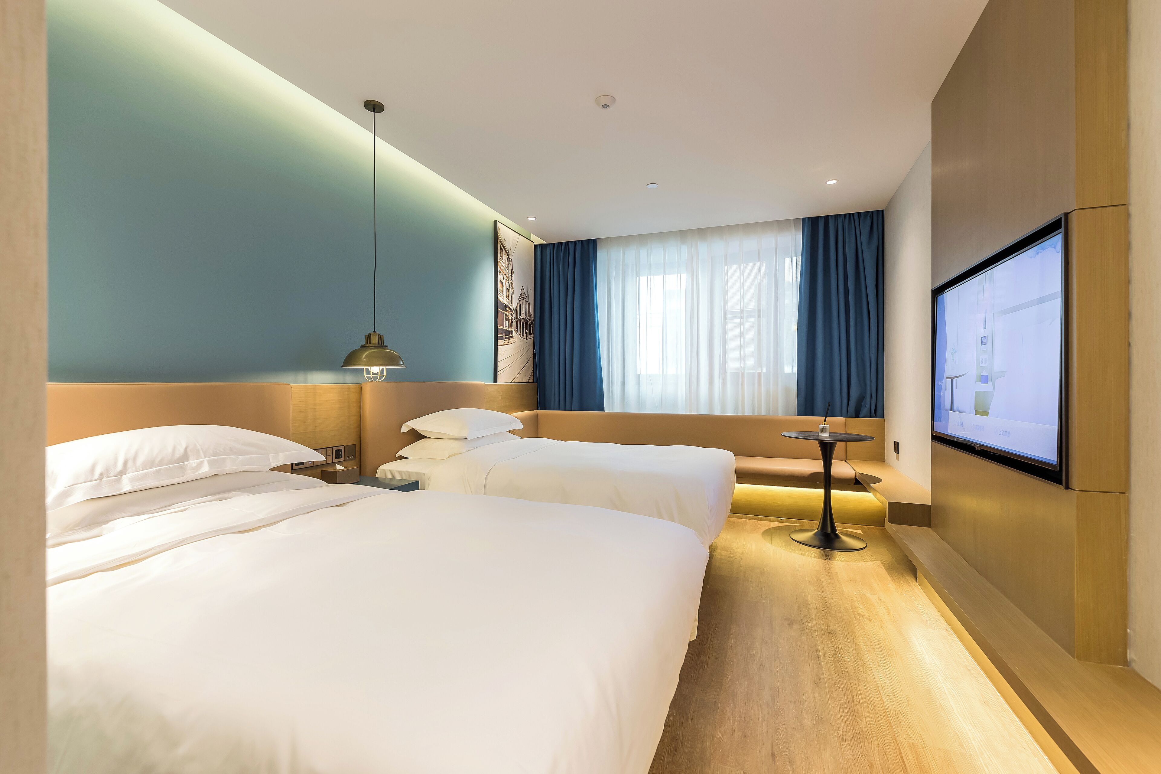 Camera d'albergo con due letti, una scrivania, una sedia, una televisione e un'ampia finestra con tende.