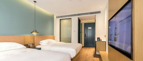 A hotel room with two beds, a TV, a bedside table, and a door leading to another room.