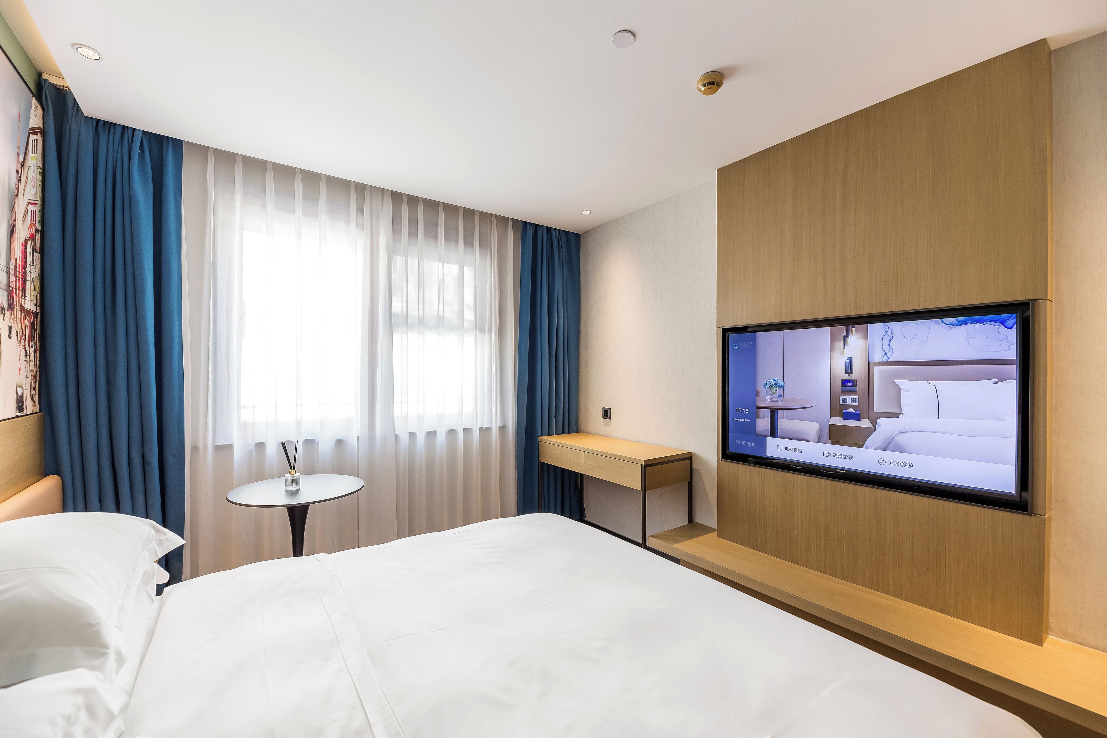Una habitación de hotel con cama, escritorio, televisión y ventana con cortinas.