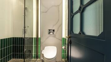 A bathroom with a white toilet, a glass shower enclosure, and green tiled walls.