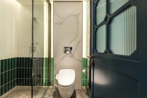 A bathroom with a white toilet, a glass shower enclosure, and green tiled walls.