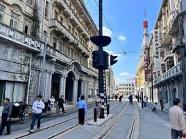 A street scene with historic buildings, a tram, and pedestrians.