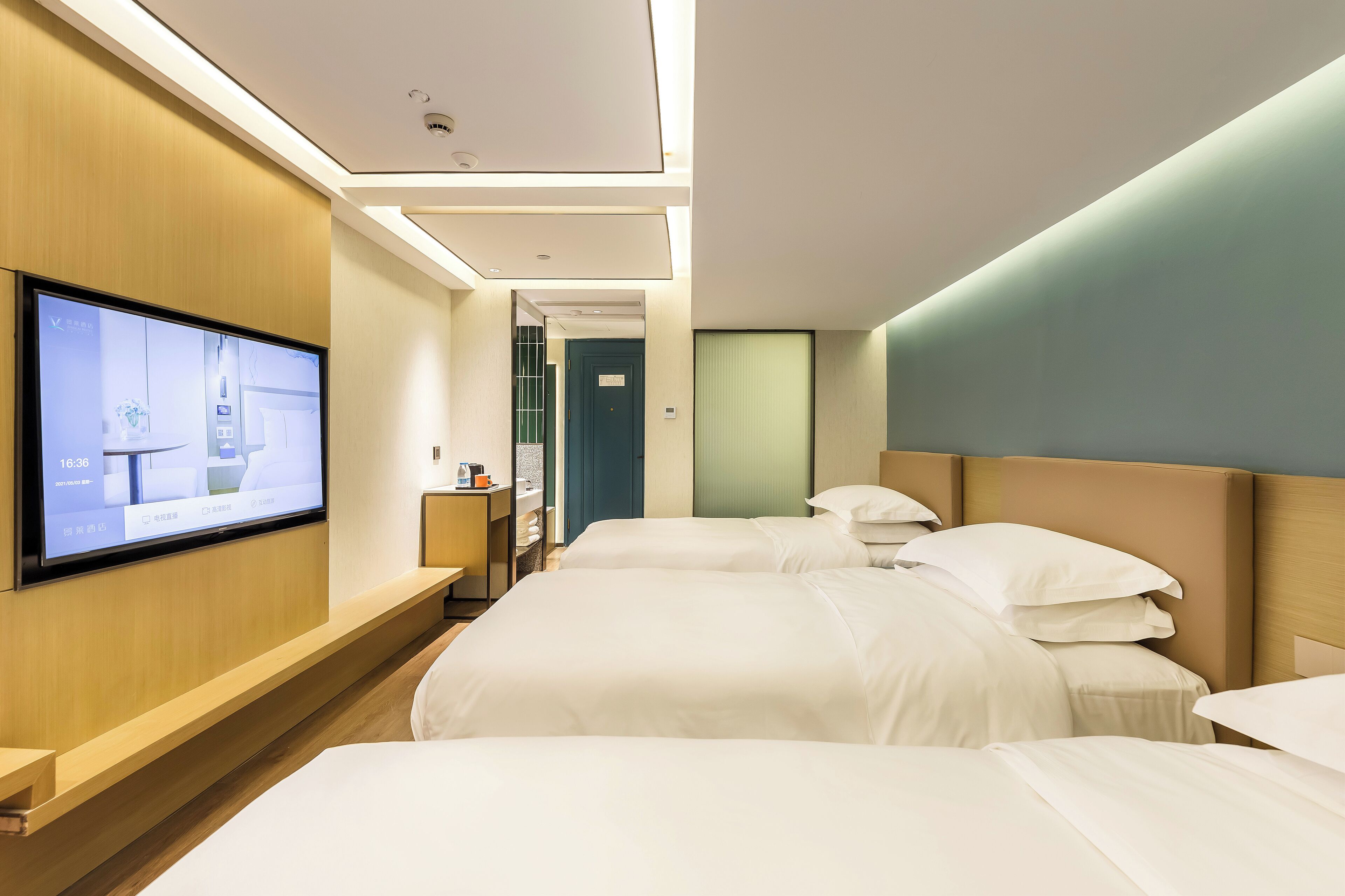 A hotel room with two beds, a TV mounted on the wall, and a wooden bench.