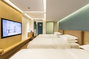 A hotel room with two beds, a TV mounted on the wall, and a wooden bench.
