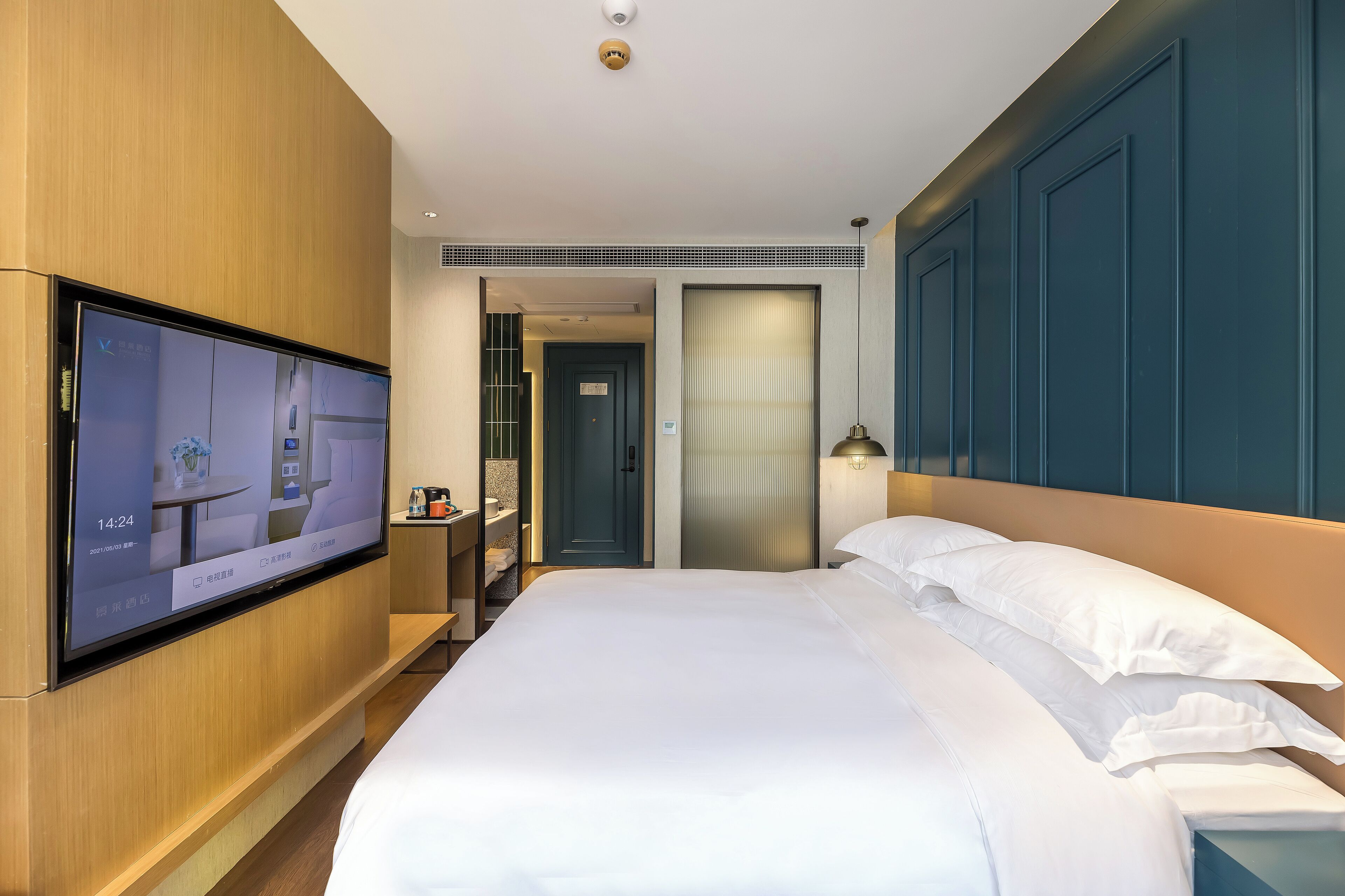 Habitación de hotel con cama, televisor montado en la pared, mesita de noche y puerta que da a otra habitación.
