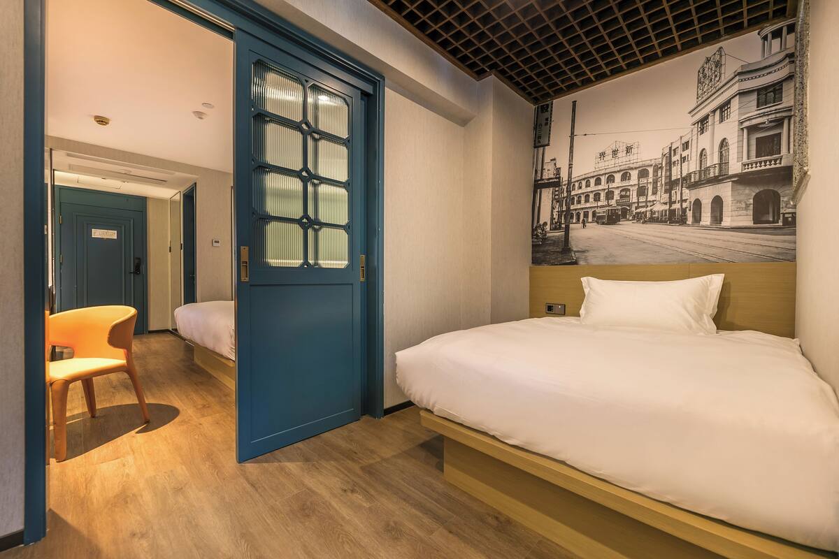 Une chambre d’hôtel avec un lit, une porte bleue, une chaise et une fresque murale.