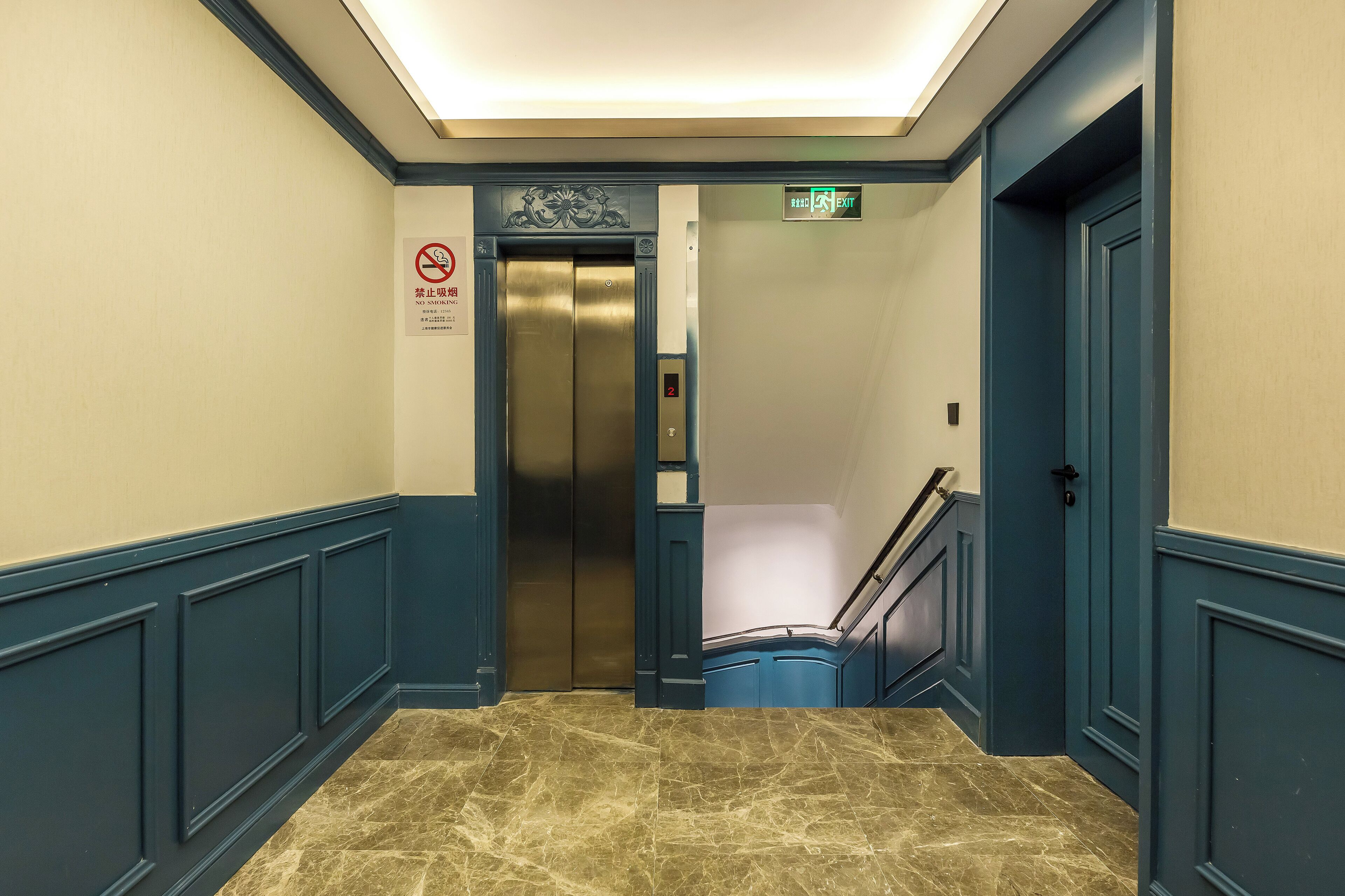 A hallway with a marble floor, blue walls, an elevator, and a staircase.