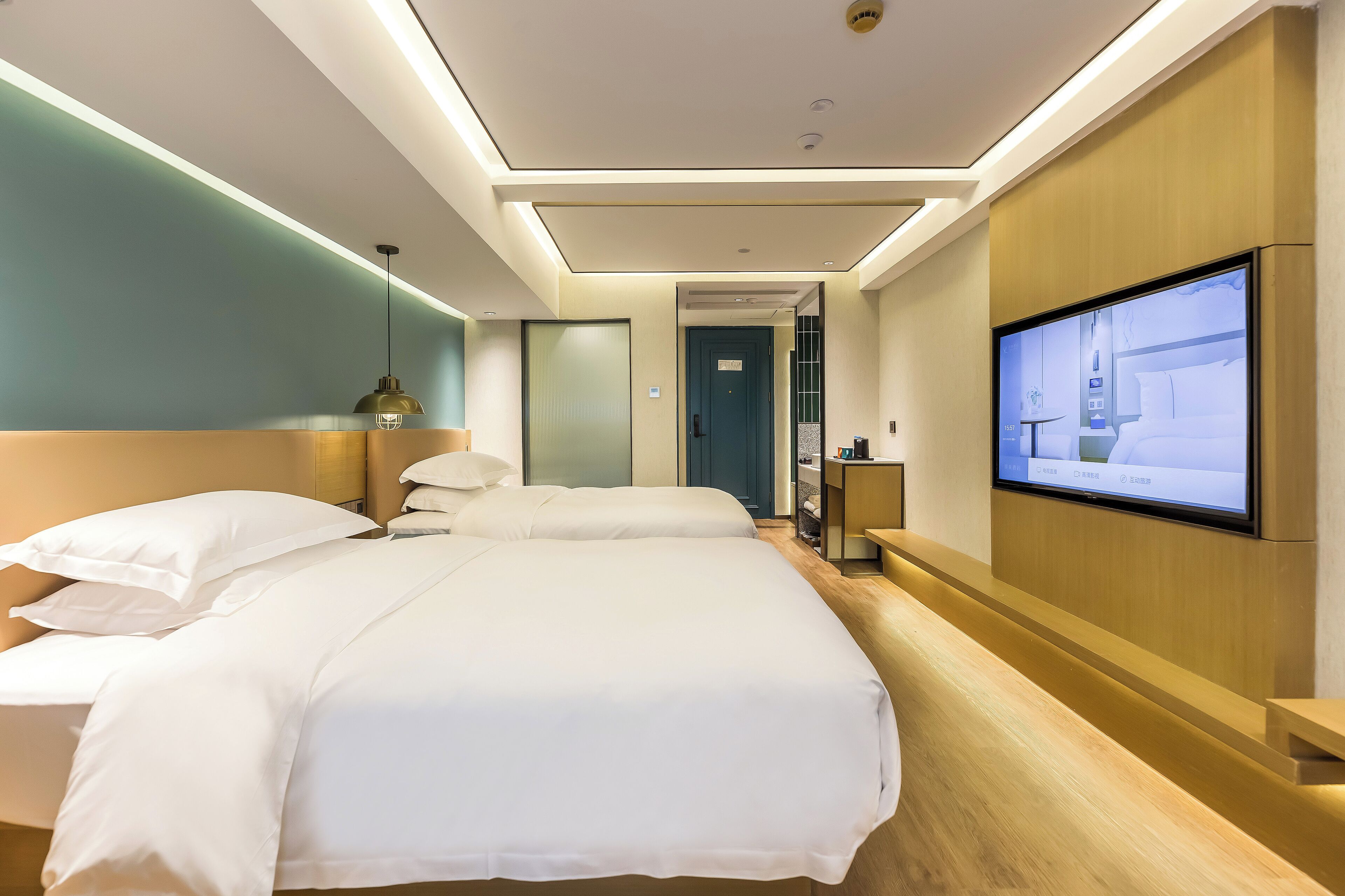 A hotel room with two beds, a TV on the wall, and a wooden reception desk.