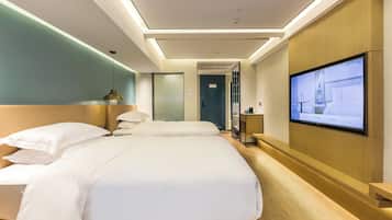 A hotel room with two beds, a TV on the wall, and a wooden reception desk.