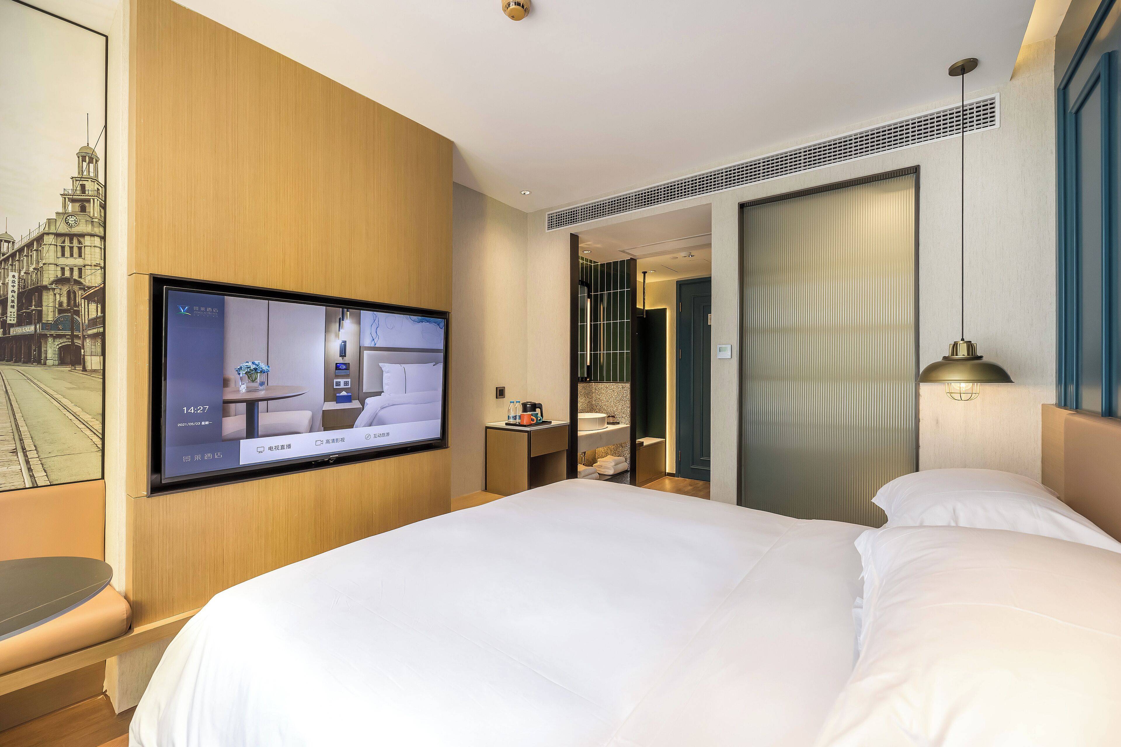 A hotel room with a large bed, a television mounted on the wall, a desk with a chair, and a bathroom visible through an open door.