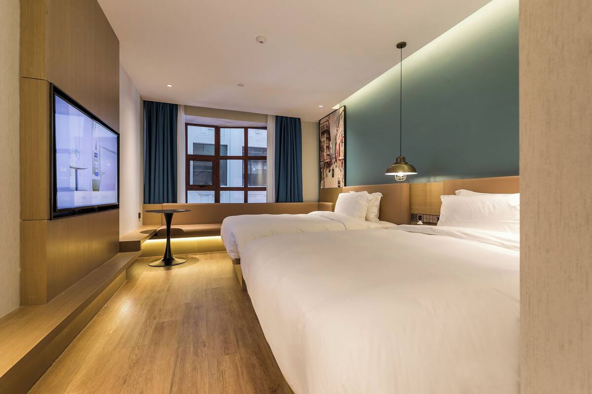 Une chambre d’hôtel avec deux lits, une télévision, un bureau et une fenêtre avec des rideaux.