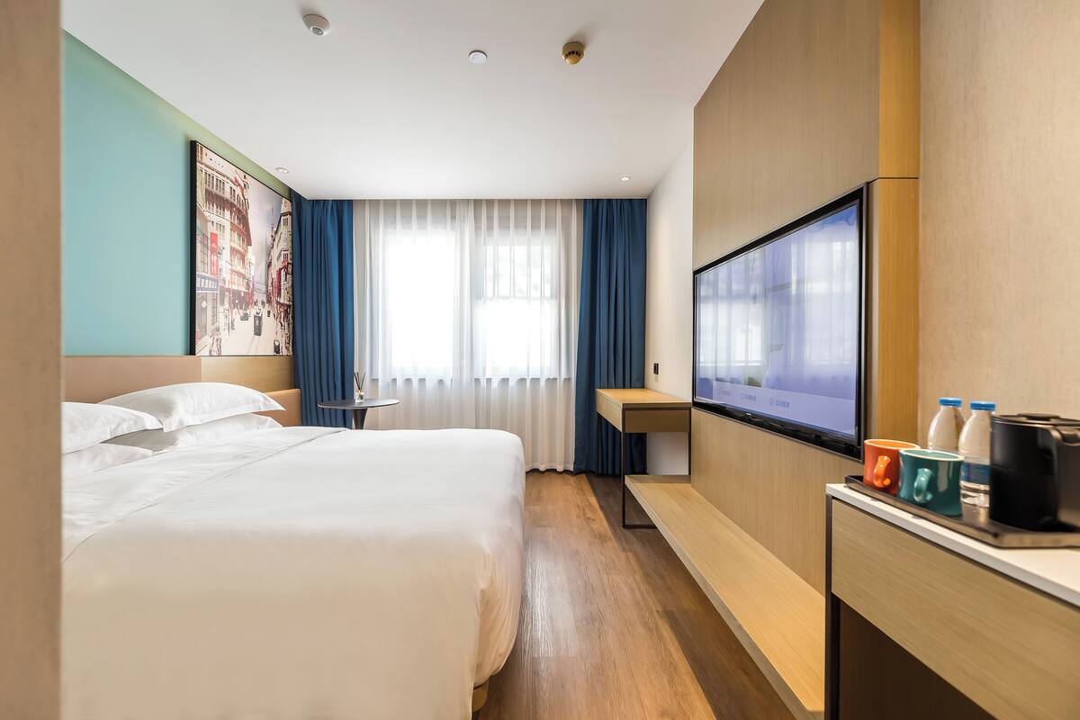 Une chambre d’hôtel avec un grand lit, un bureau doté d’une télévision à écran plat, une machine à café et une fenêtre avec des rideaux.
