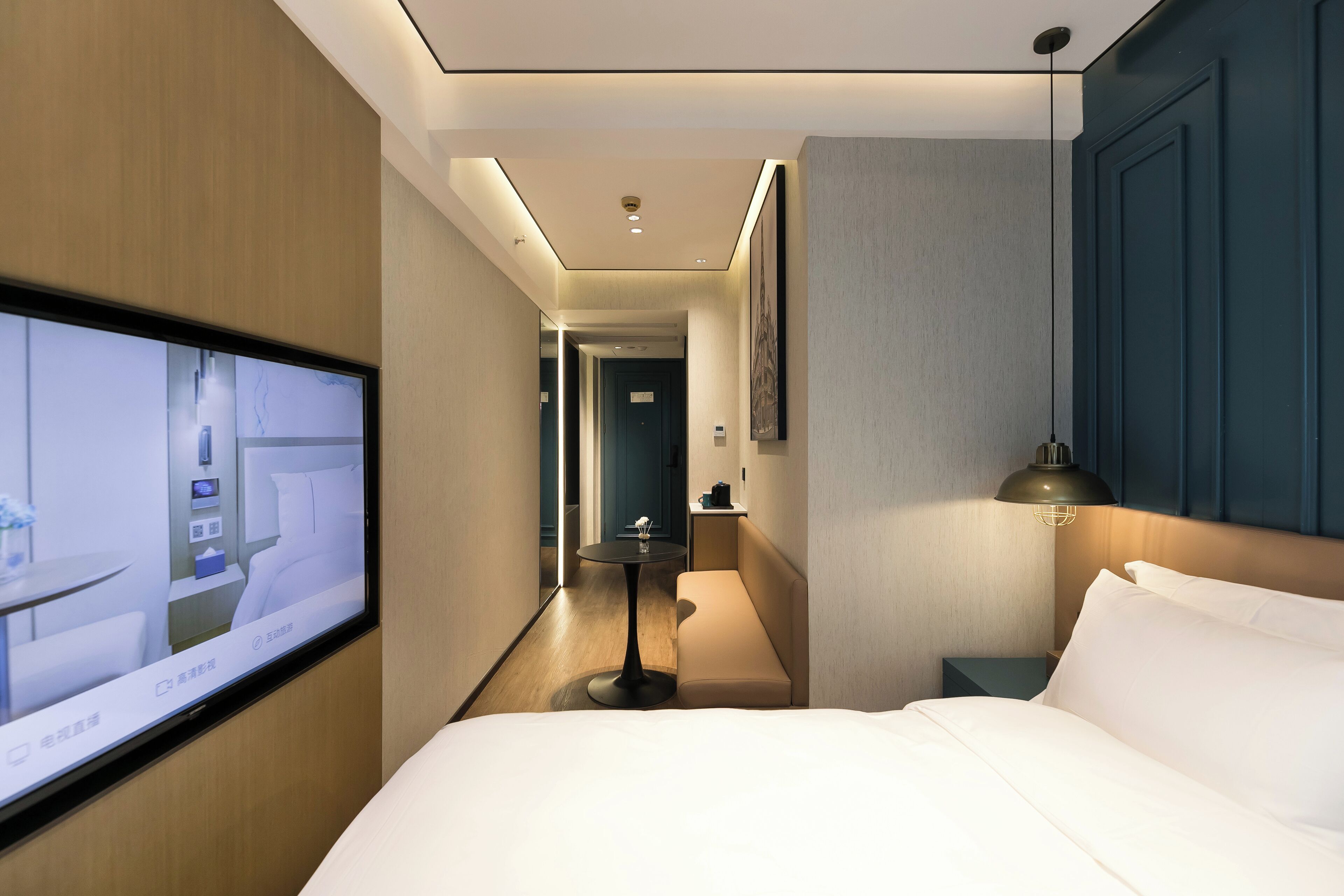 Une chambre d’hôtel avec un lit, un téléviseur fixé au mur, une table de chevet et une lampe.