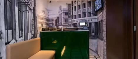 A hotel lobby with a mural of a cityscape, a reception desk, a green partition, and a beige sofa.