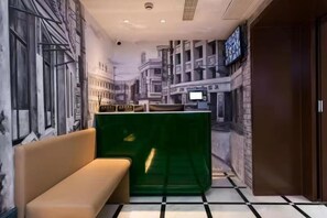 A hotel lobby with a mural of a cityscape, a reception desk, a green partition, and a beige sofa. - Jinglai Hotel (Shanghai Bund East Nanjing Road Pedestrian Street) (Shanghai)