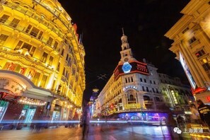 A historic building with a clock tower and illuminated signage, surrounded by other buildings and a pedestrian area. - Jinglai Hotel (Shanghai Bund East Nanjing Road Pedestrian Street) (Shanghai)