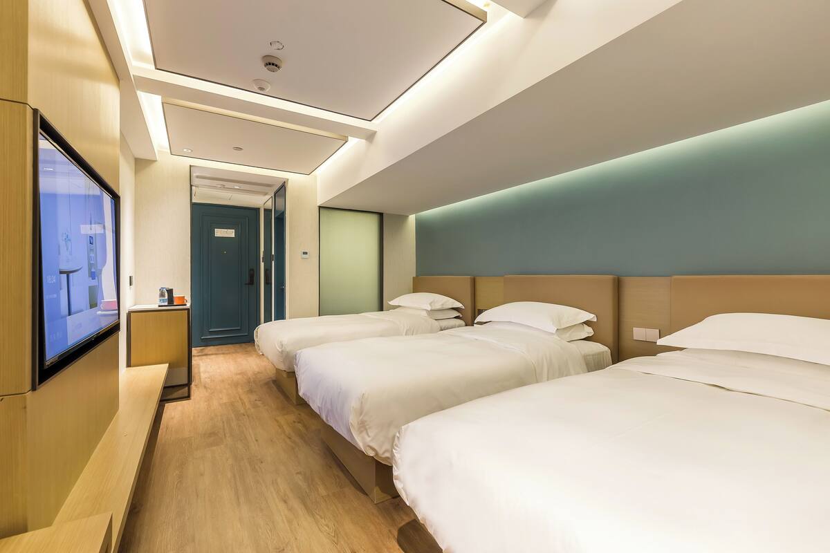 Une chambre d’hôtel avec trois lits, un téléviseur fixé au mur et un plancher en bois.