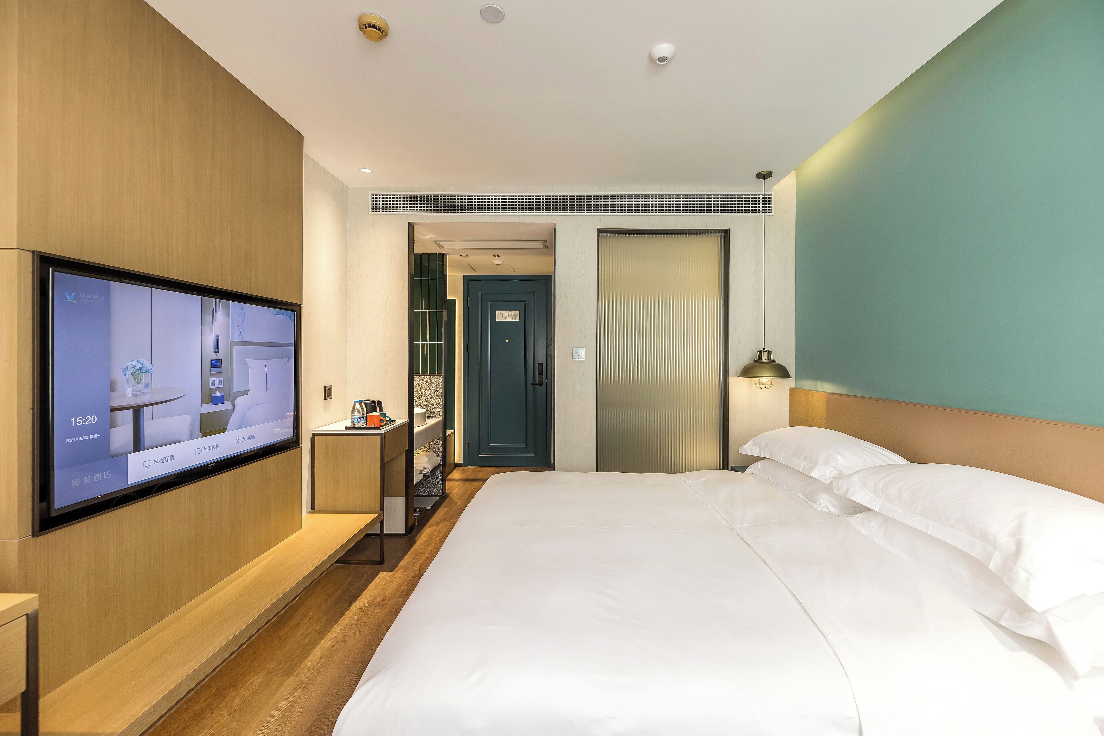 Une chambre d’hôtel moderne dotée d’un grand lit, d’un téléviseur fixé au mur, d’un bureau avec une chaise et d’une salle de bain visible à travers une porte ouverte.