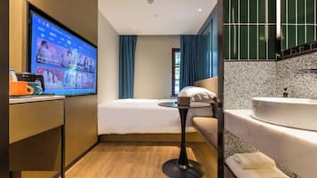 Een moderne hotelkamer met een bed, een klein rond tafeltje, een televisie, een badkamer met wastafel en spiegel, en houten vloeren.