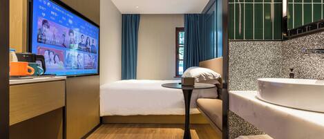 A modern hotel room with a bed, a small round table, a TV, a bathroom with a sink and mirror, and wooden flooring.