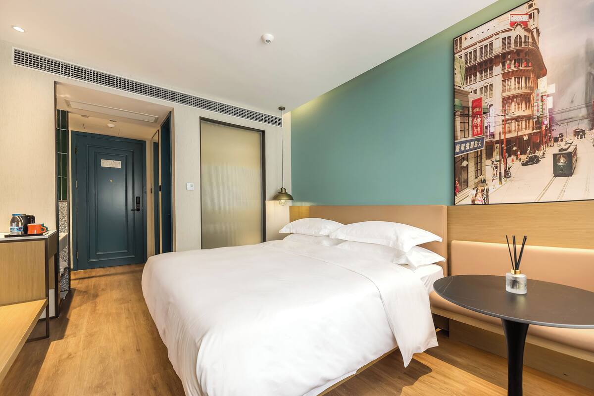 Une chambre d’hôtel avec un lit, une table de chevet, une lampe fixée au mur, une petite table ronde et une grande affiche accrochée au mur.