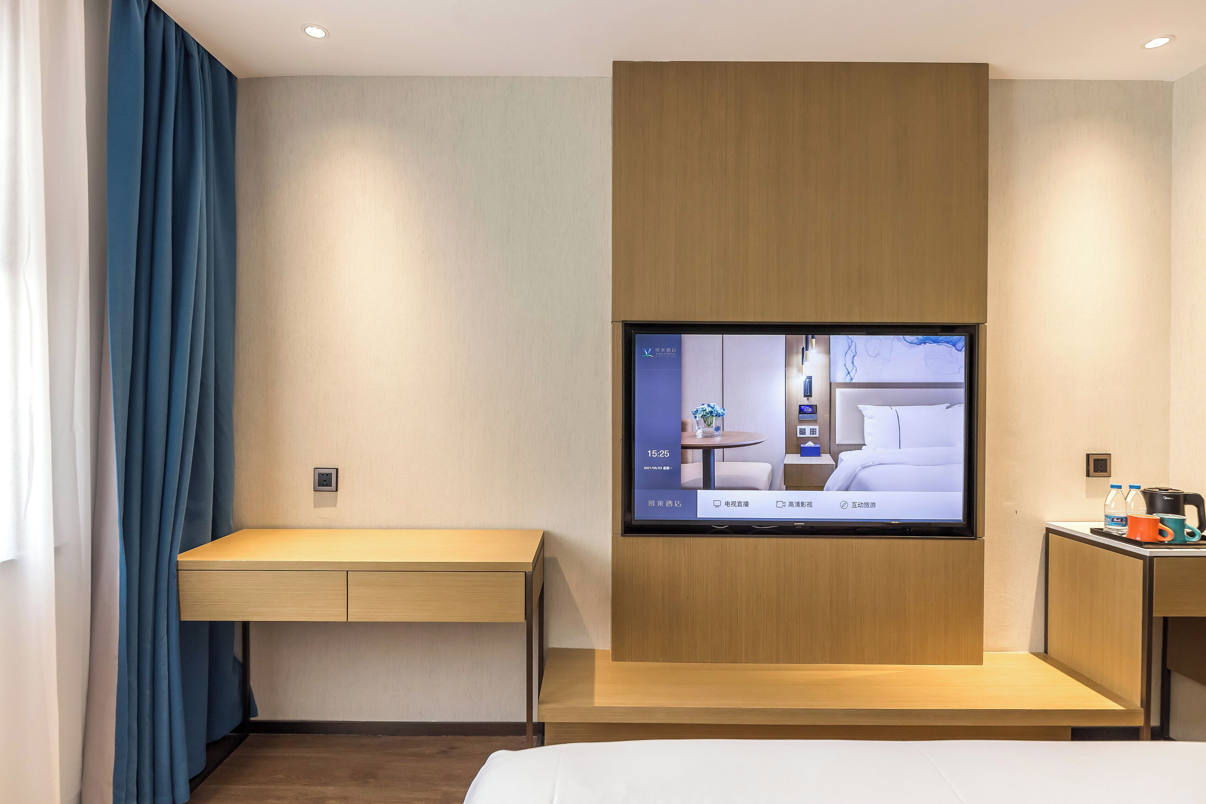 A hotel room with a flat-screen TV mounted on the wall, a wooden desk, a bed, and a small table with a coffee maker.