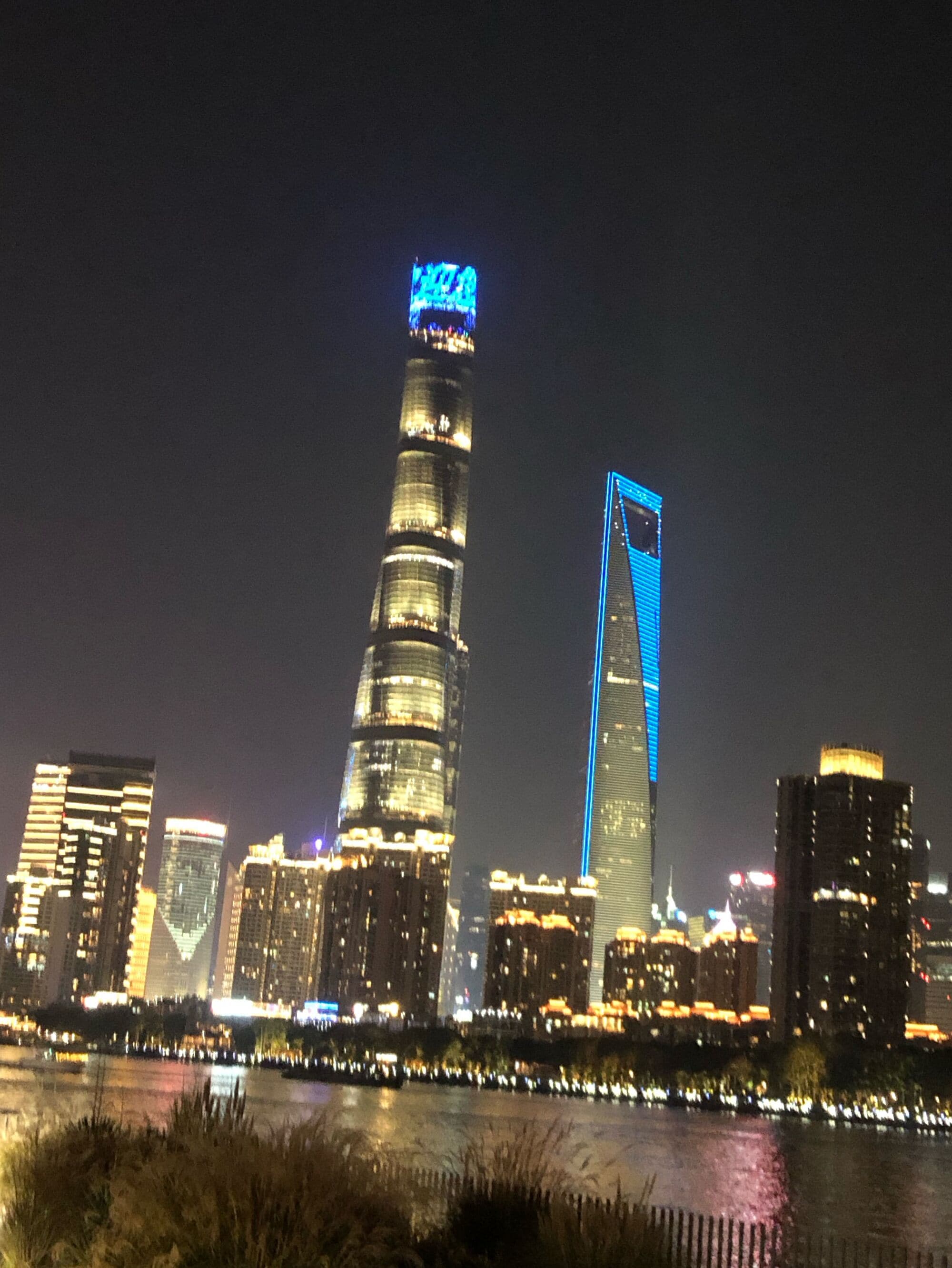 A city skyline at night with illuminated buildings, including a prominent tower with a blue-lit top.