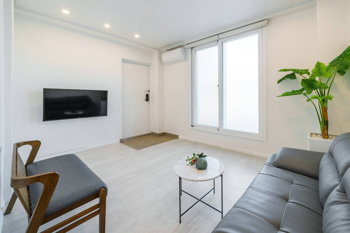Ein modernes Wohnzimmer mit einem grauen Sofa, einem Holzstuhl, einem kleinen runden Tisch und einem flachbildfernseher an der Wand.