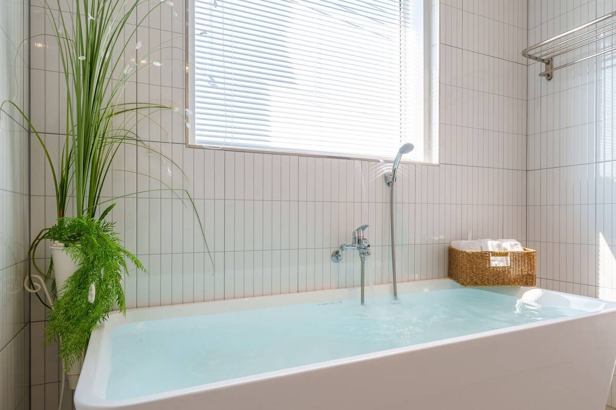 Ein modernes Badezimmer mit einer freistehenden Badewanne, einer Duschbrause und einem Fenster mit Jalousien.