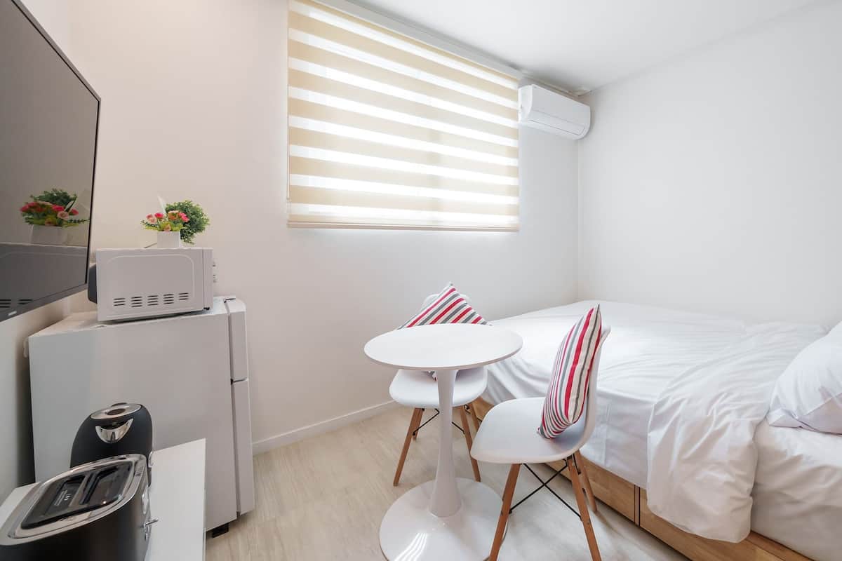 Ein kompaktes Hotelzimmer mit einem Einzelbett, einem kleinen Tisch, einem Stuhl, einem Fernseher und einer Küchenzeile.