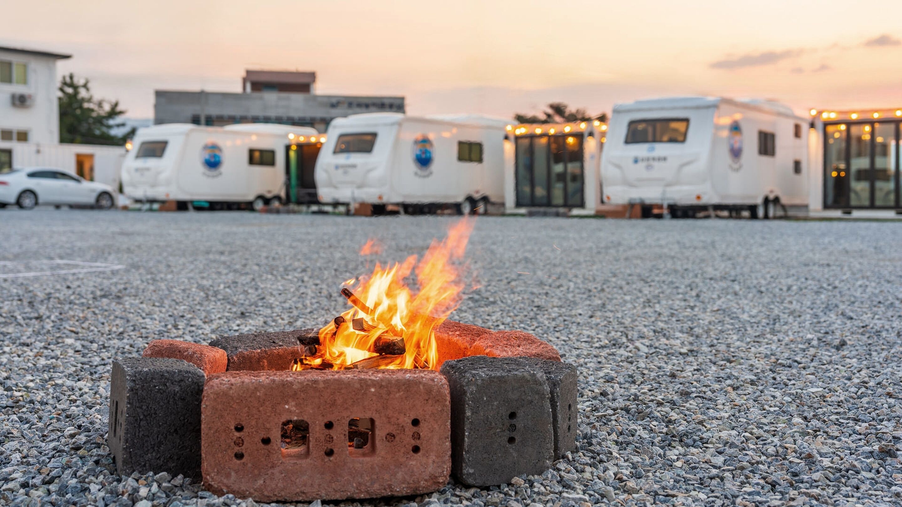 A campfire in a gravel area with RVs in the background.