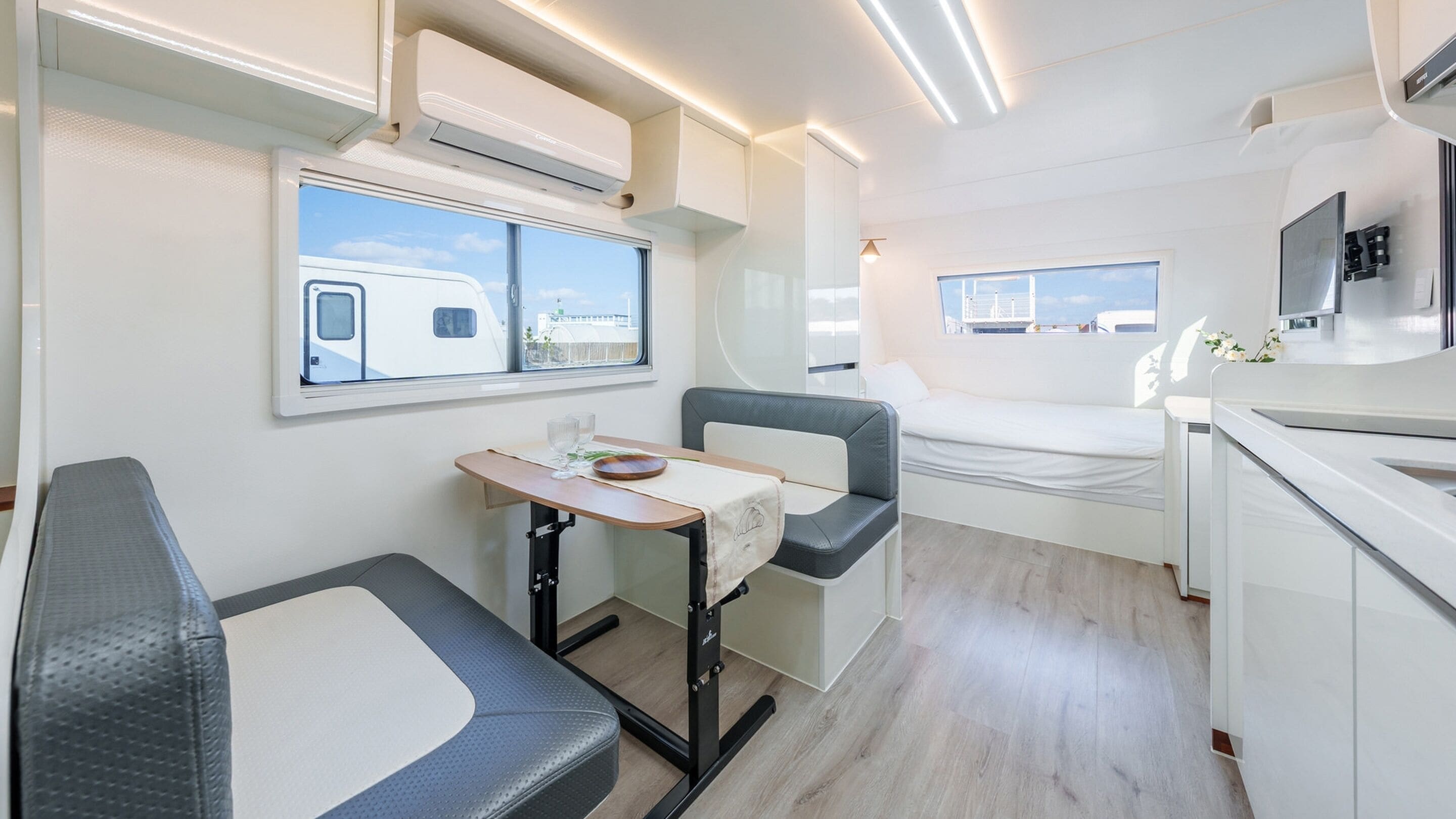 Een compact camperinterieur met een kitchenette, een eethoek en een slaapgedeelte.