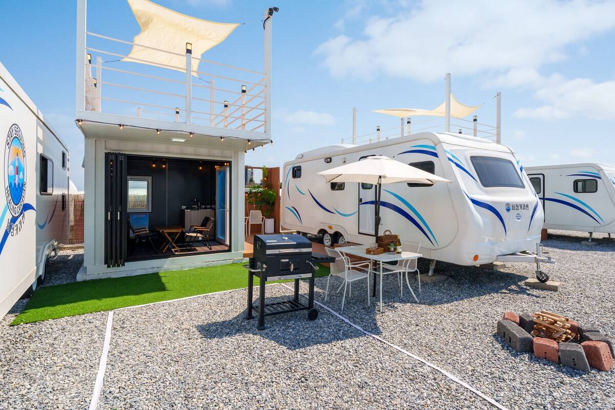 Un camping abritant plusieurs caravanes, un espace barbecue et un petit bâtiment doté d’une porte en verre.
