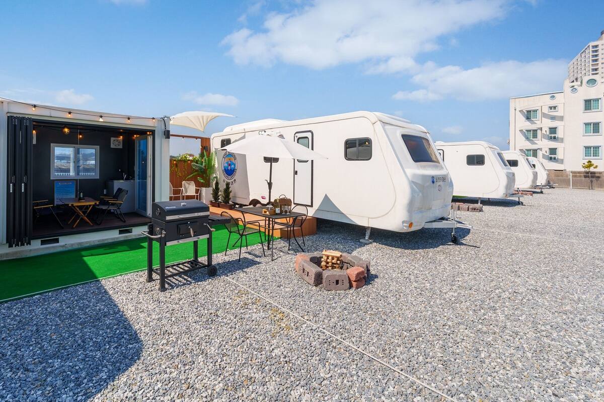 Une caravane équipée d’un coin repas, d’un barbecue et d’un petit jardin.