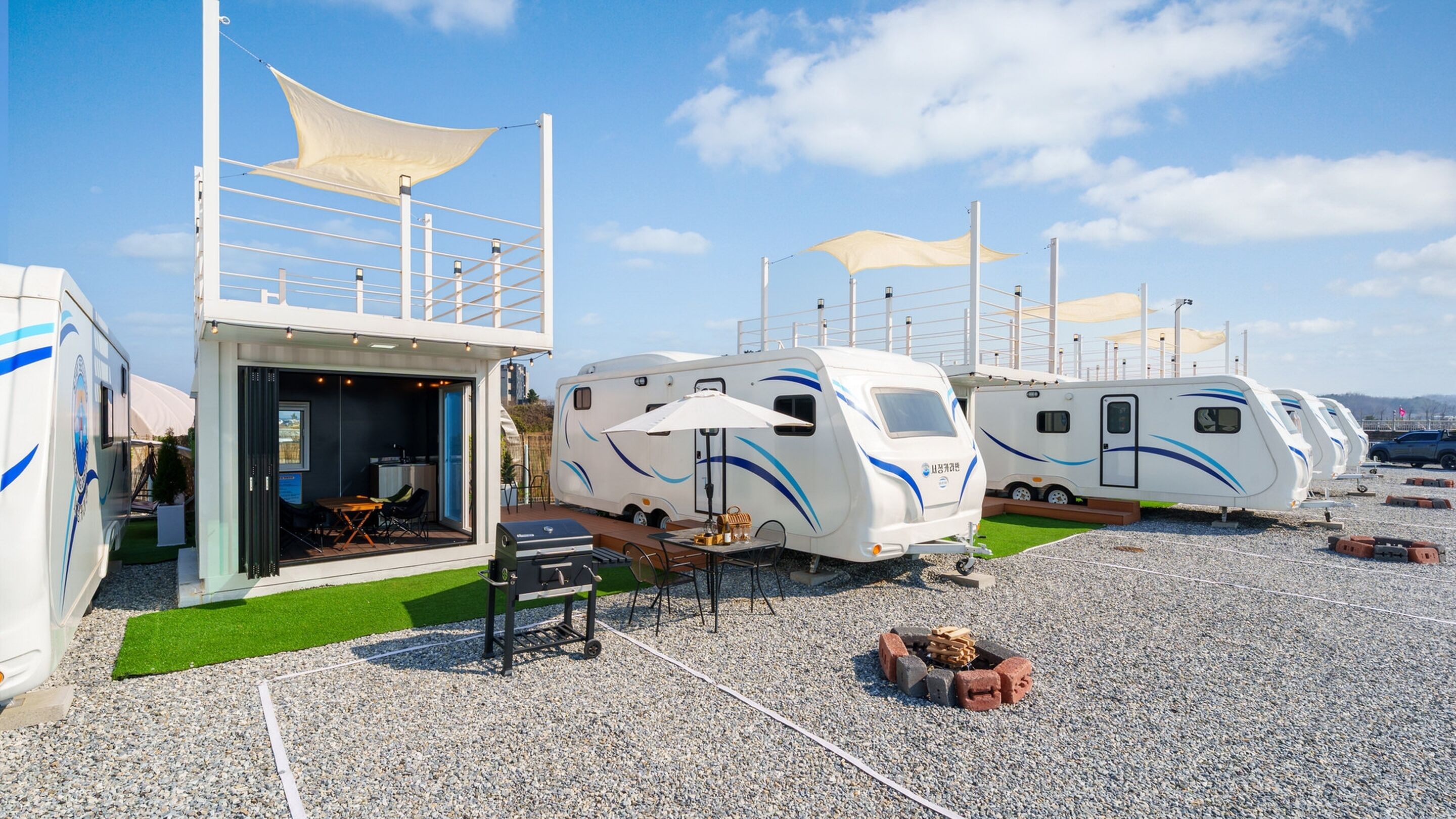 A row of RVs with outdoor dining areas, a barbecue grill, and a covered seating area.