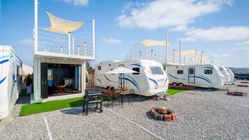 A row of RVs with outdoor dining areas, a barbecue grill, and a covered seating area.