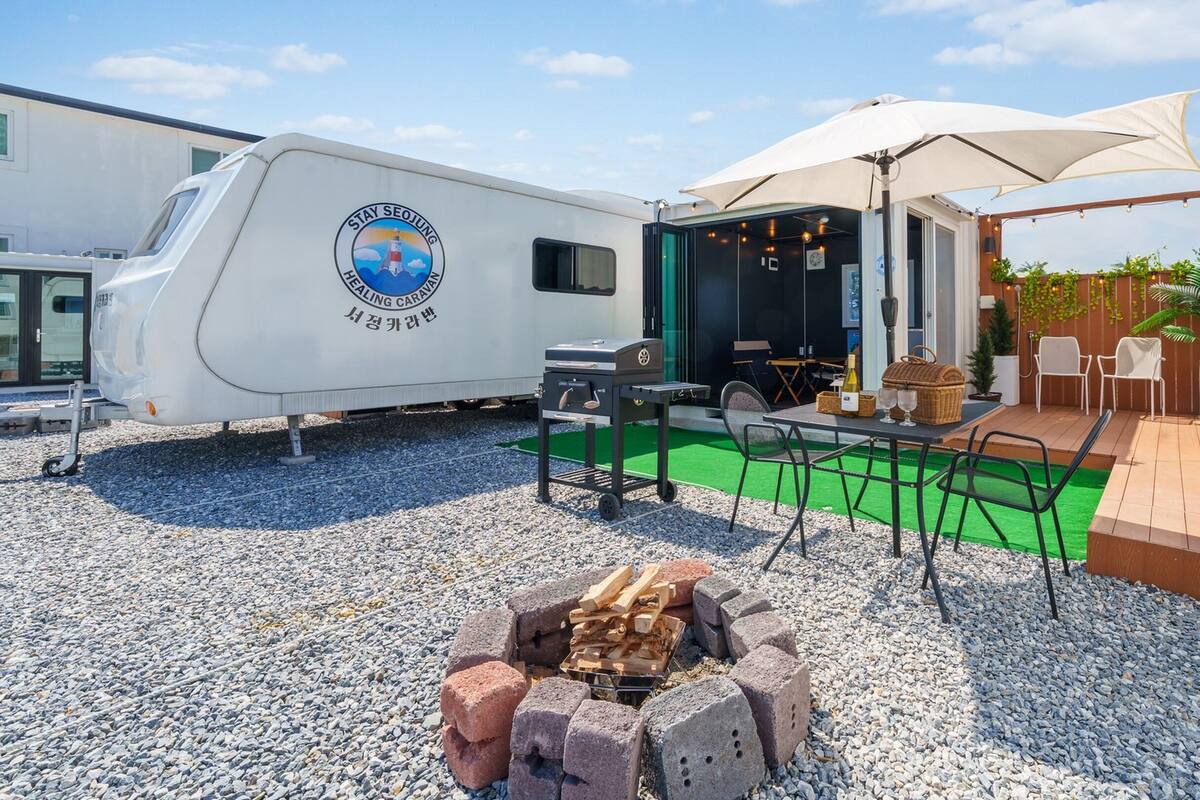 Une caravane arborant le logo « Stay Seojung », dotée d’un espace barbecue et d’une terrasse avec des sièges d’extérieur.